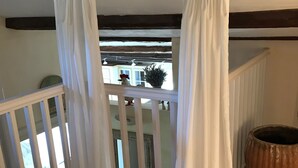 Een slaapkamer met een bed, een balkon met een leuning, een plant in een pot en een houten vat.