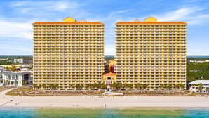 Ein Strandhotel mit zwei markanten, gelben Gebäuden, einem sandigen Strand und einem strahlend blauen Himmel.