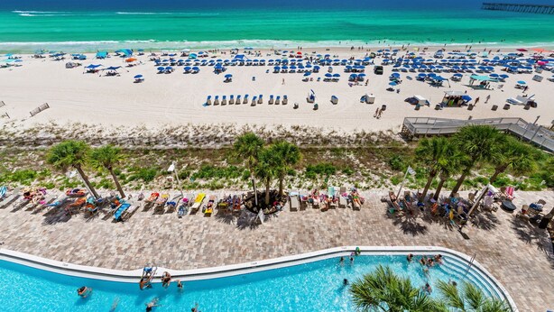 Ein Strandresort mit Schwimmbad, Strandliegen und Sonnenschirmen.