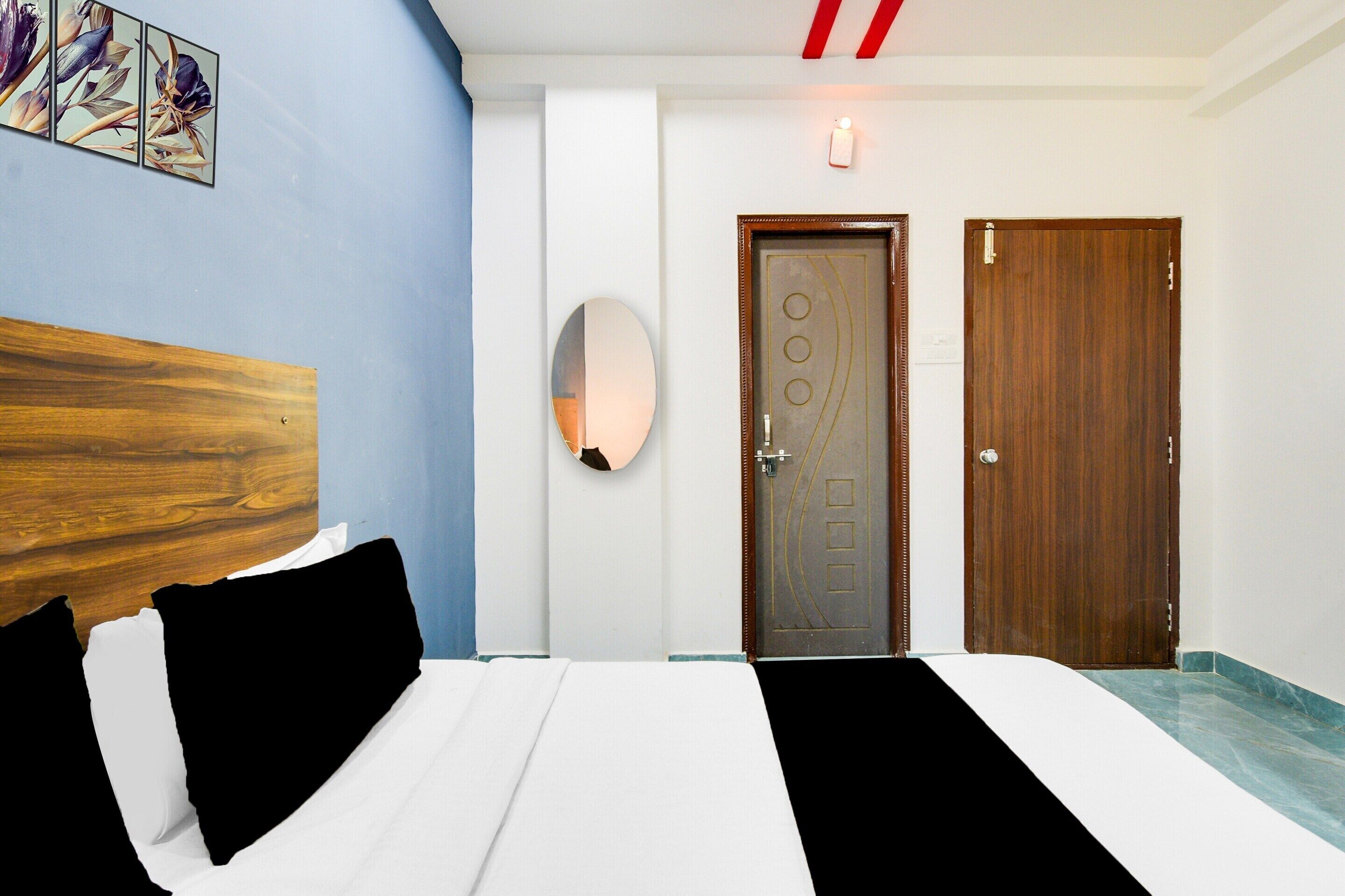 A hotel room with a bed, a wooden headboard, a wall-mounted light, and two doors.