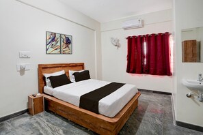 Quarto de hotel com cama de madeira, mesa de cabeceira pequena, ar condicionado fixado na parede, cortina vermelha, espelho e pia.