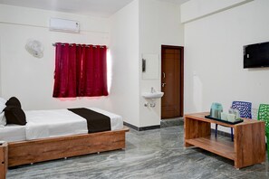 Quarto com cama, mesa de cabeceira de madeira, pia, espelho, televisão e janela com cortinas vermelhas.