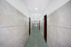 A corridor with marble walls and doors, leading to a room with a green floor. - Deluxe Hotel O Sunkadakatte (Bengaluru)