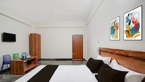 A hotel room with a bed, a wooden headboard, a television, a wooden cabinet, two chairs, and two framed artworks on the wall. - Deluxe Hotel O Sunkadakatte (Bengaluru)