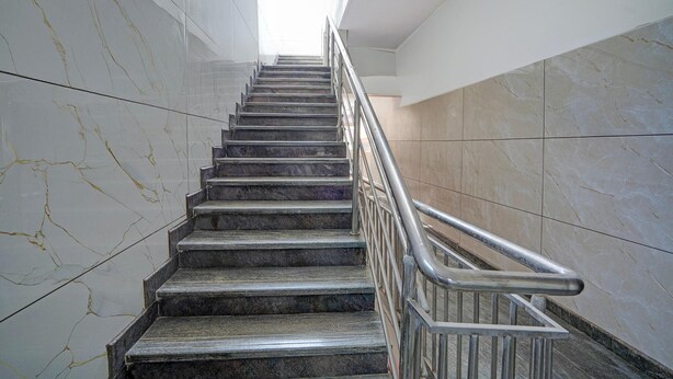 A marble staircase with metal railings, leading upwards in a modern building. - Deluxe Hotel O Sunkadakatte (Bengaluru)