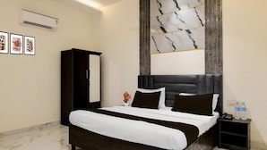A hotel room with a large bed, a dark headboard, a nightstand with a phone and water bottles, and a wall-mounted air conditioner. - Deluxe GT Road Amritsar (Amritsar)