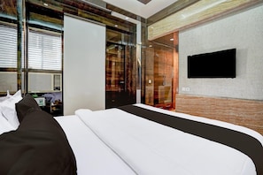 A modern hotel room with a large bed, a TV mounted on the wall, and a glass door leading to a bathroom. - Deluxehotel Shanti Kutir (Kanpur)