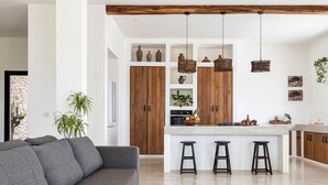 A modern kitchen with wooden cabinets, a central island with stools, and hanging lights.