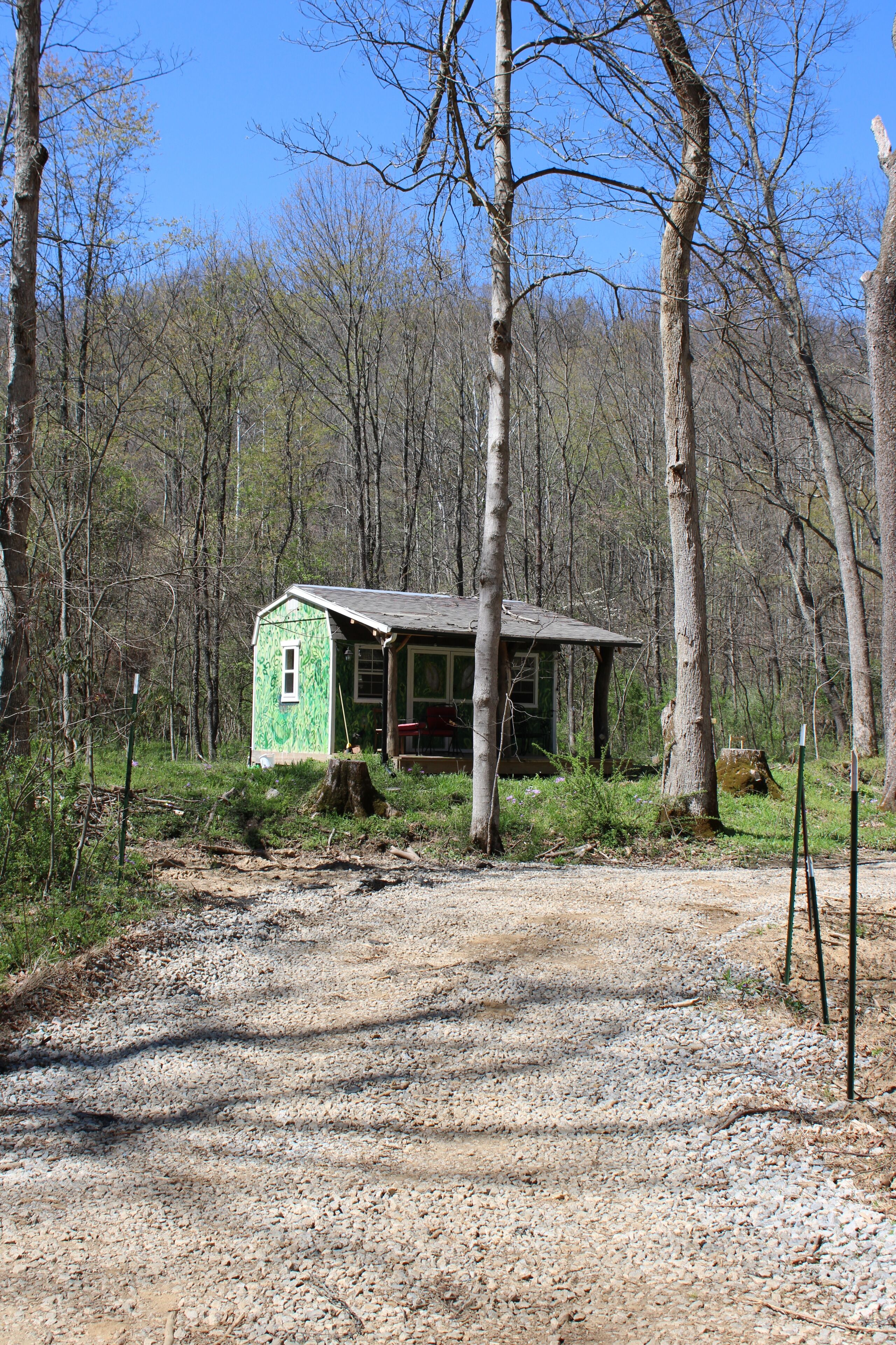 A small cabin with a green exterior, surrounded by trees and a gravel path.