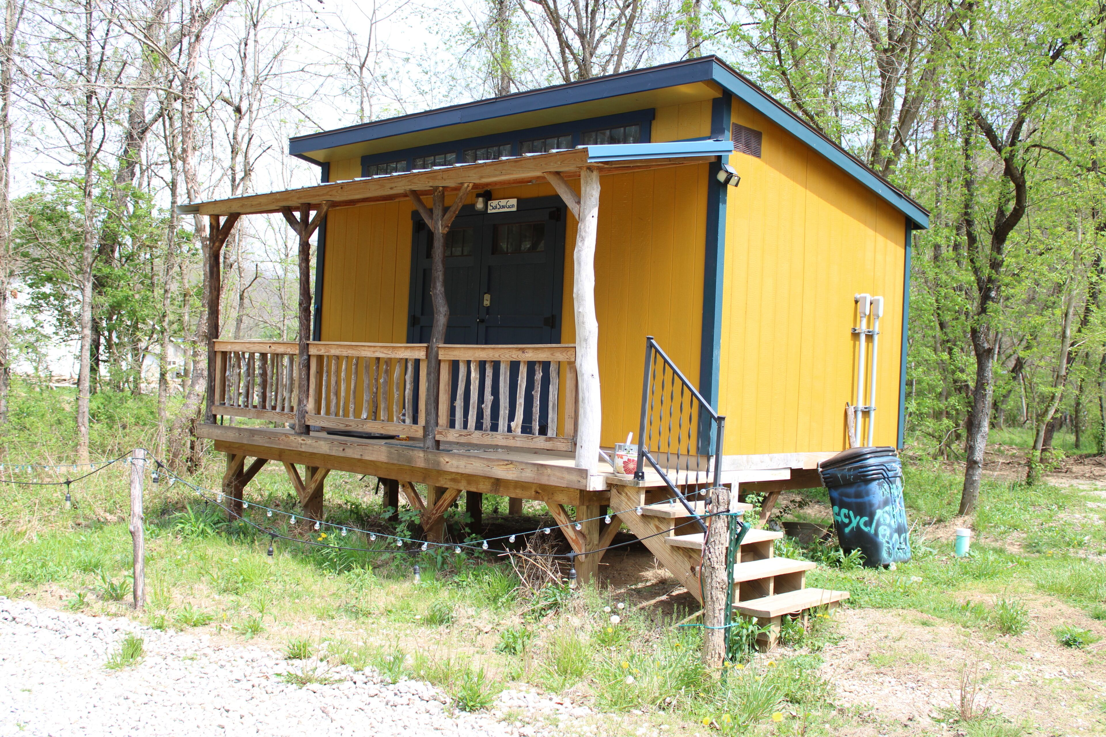 A yellow cabin with a wooden deck and a porch, surrounded by trees.