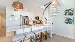 Una cocina moderna con una isla central, taburetes de bar, un refrigerador de acero inoxidable y una original escalera en espiral.