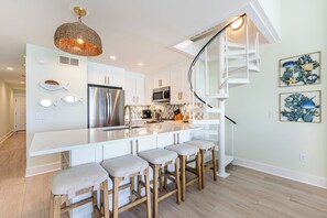 Eine moderne Küche mit Kochinsel, Barhocker, einem Edelstahlkühlschrank und einer außergewöhnlichen Wendeltreppe.