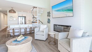 Una sala de estar moderna con chimenea, un comedor con taburetes de bar y una cocina con armarios blancos y una escalera en espiral.