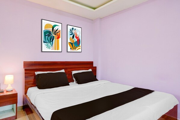 A hotel room with a wooden headboard, a bed with white and black bedding, two framed abstract artworks on the wall, and a nightstand with a lamp.