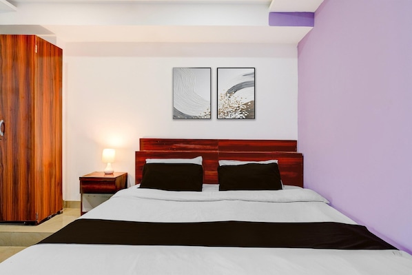 A bedroom with a bed, a nightstand, a wooden wardrobe, and two wall-mounted artworks.