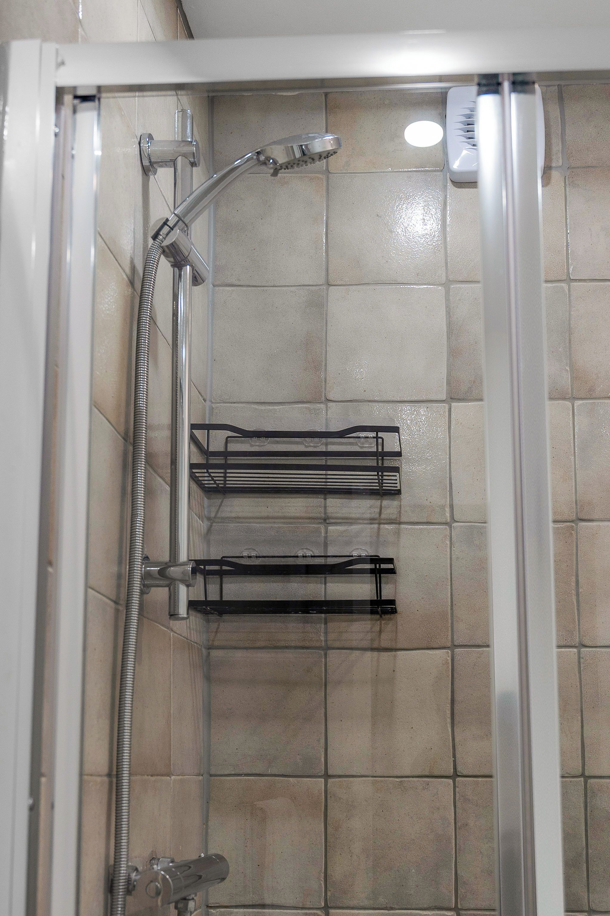A shower enclosure with a handheld showerhead, a wall-mounted towel rack, and a glass door.