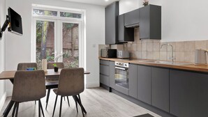 A modern kitchen with grey cabinets, a wooden countertop, and a dining area with chairs. - Cosy 2 Bed-5 Guests-garden-parking&wifi (London)