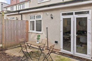 A residential property with a patio, a wooden fence, a table with chairs, a potted plant, and a sliding glass door. - Cosy 2 Bed-5 Guests-garden-parking&wifi (London)