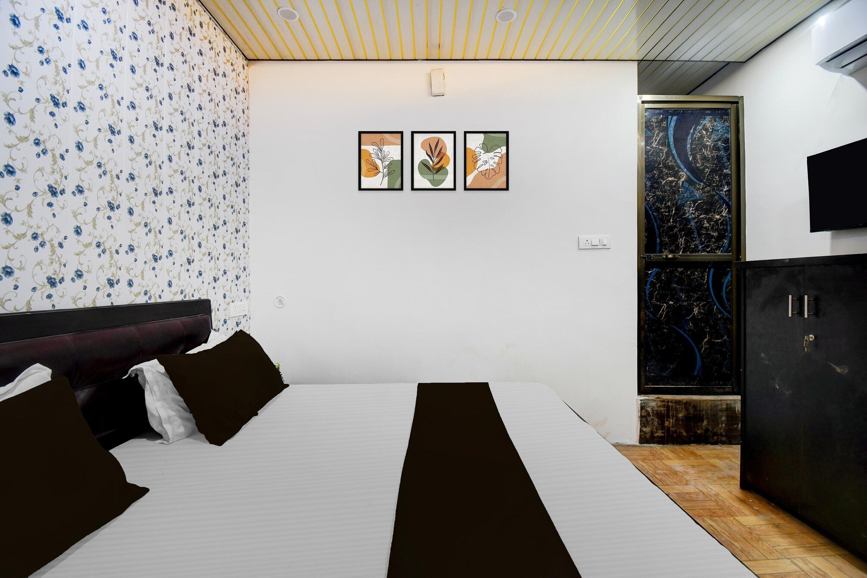 Un dormitorio con una cama, un televisor montado en la pared y tres obras de arte enmarcadas.