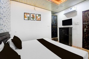 A hotel room with a bed, a flat-screen TV mounted on the wall, an air conditioning unit, and a dark-colored cabinet. - Deluxehotel Mayur Residency (Gorakhpur)