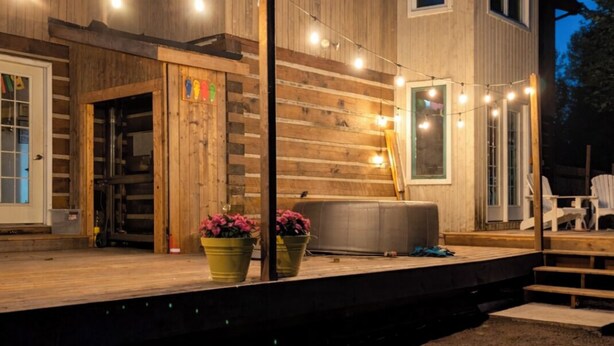 Une maison en bois avec un porche, des guirlandes lumineuses et des plantes en pot.
