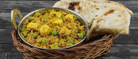 A dish of paneer curry with peas and naan bread on a rustic wooden table.