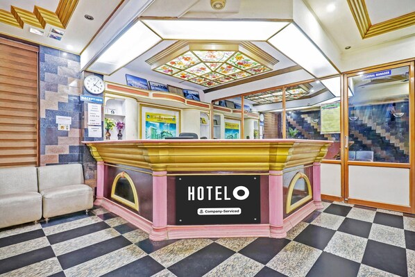 A reception area with a check-in counter, a clock, and a sign indicating 'HOTELO' and 'Company-Serviced.'