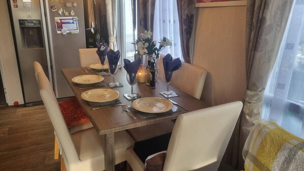 A dining table set with plates, glasses, and a vase of flowers. - Villa With Decking & Parking (Clacton-on-Sea)