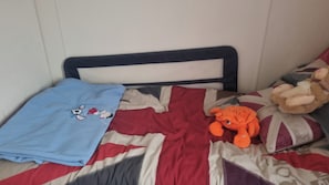 Una cama con una colcha azul, un edredón blanco y rojo y un peluche.