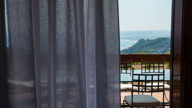A balcony with a table and chairs, overlooking a coastal landscape.