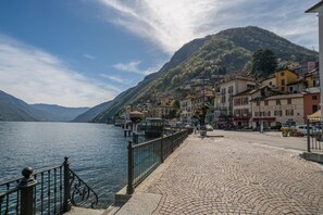 Eine Uferpromenade aus Kopfsteinpflaster mit Gebäuden, Bergen im Hintergrund und blauem Himmel.
