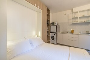 Ein Schlafzimmer mit Bett, Waschmaschine und einer Küchenzeile mit Schränken und Mikrowelle.