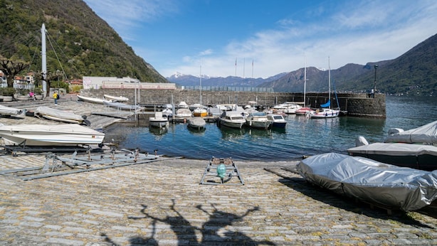 Un puerto deportivo con barcos amarrados, un muelle de piedra y montañas al fondo.