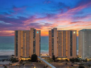 Een hoog hotel met meerdere verdiepingen, uitzicht op het strand en een zonsondergang.