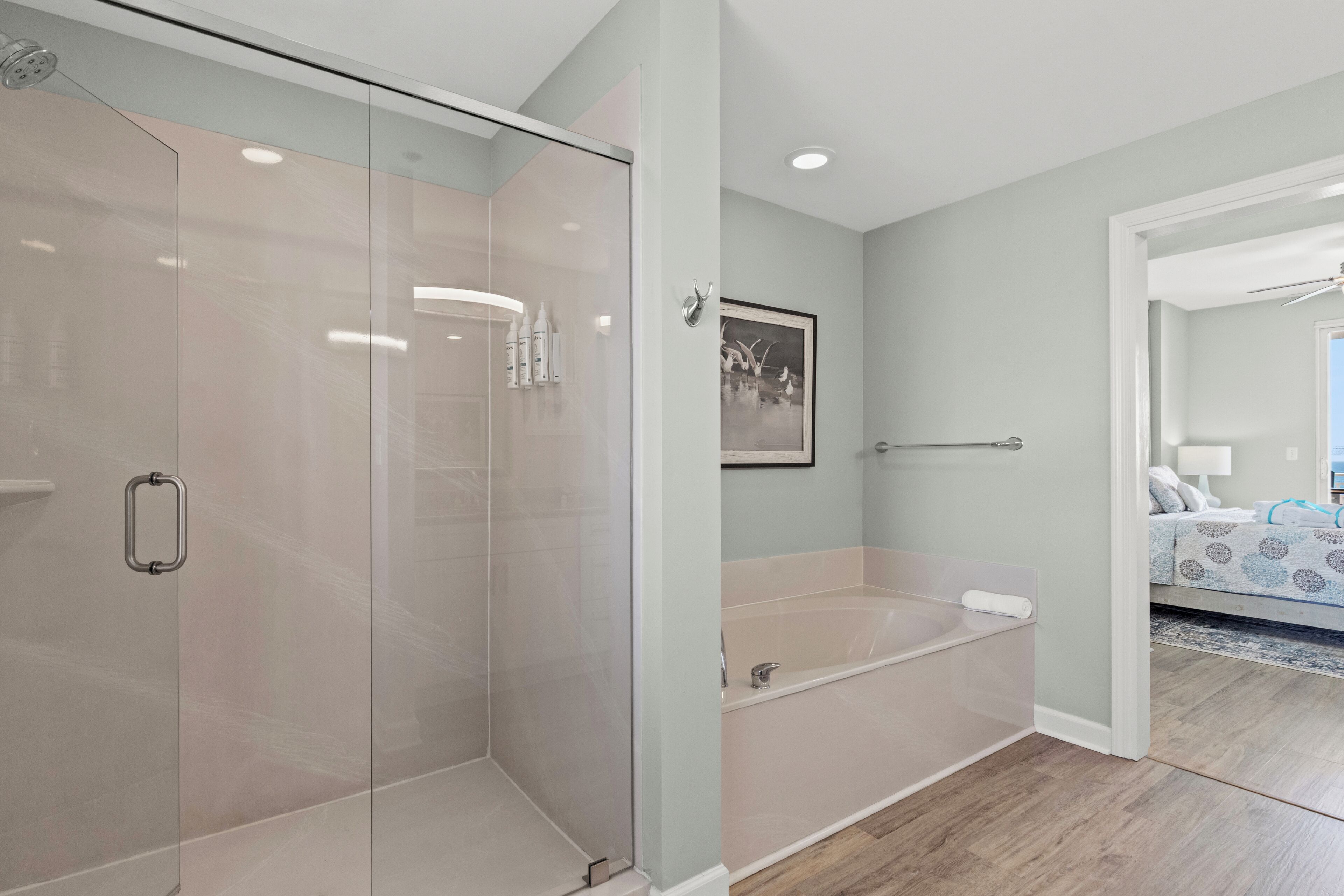 Une salle de bain moderne dotée d’une douche à parois de verre, d’une baignoire et d’une porte visible donnant sur une chambre.