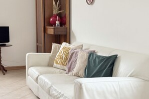 A white leather sofa with multiple cushions, a small wooden side table with a remote control, and a television on the left. - SE244 - Senigallia, large four-room apartment  (Senigallia)