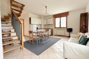 A modern kitchen with white cabinets, a dining area with a table and chairs, a staircase, a white sofa, and a radiator. - SE244 - Senigallia, large four-room apartment  (Senigallia)