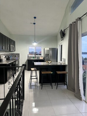 Eine moderne Küche mit einer großen Kochinsel, Barhocker, einer Pendelleuchte und Blick durch das Fenster.