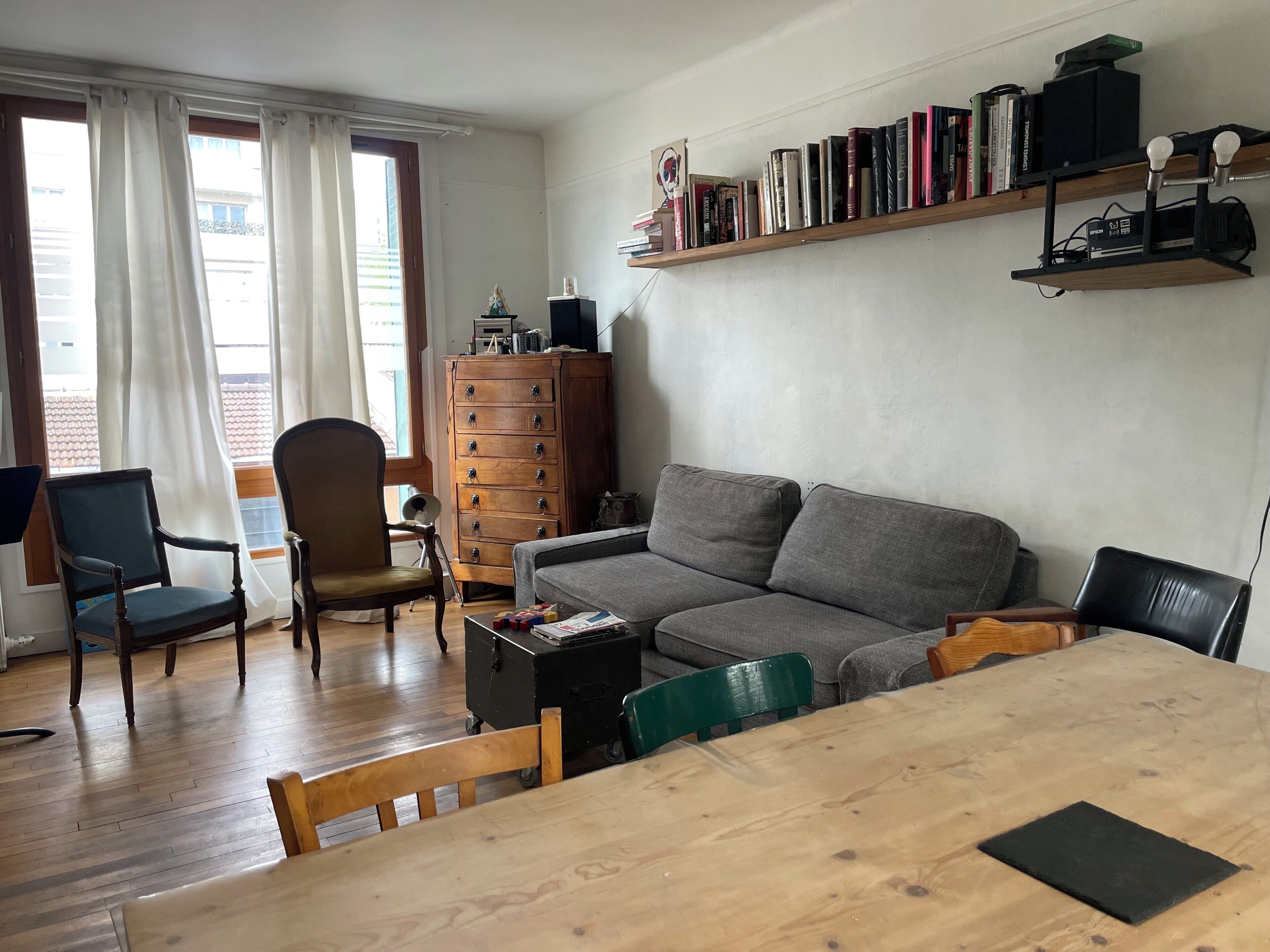 A living room with a wooden table, grey sofa, wooden cabinet, and a bookshelf with books.