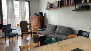 En stue med et træbord, en grå sofa, et træskab og en reol fyldt med bøger.