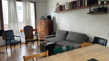 A living room with a wooden table, grey sofa, wooden cabinet, and a bookshelf with books.