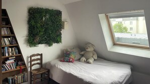 Et soveværelse med seng, stol, bogreol, vægplante og en bamse.