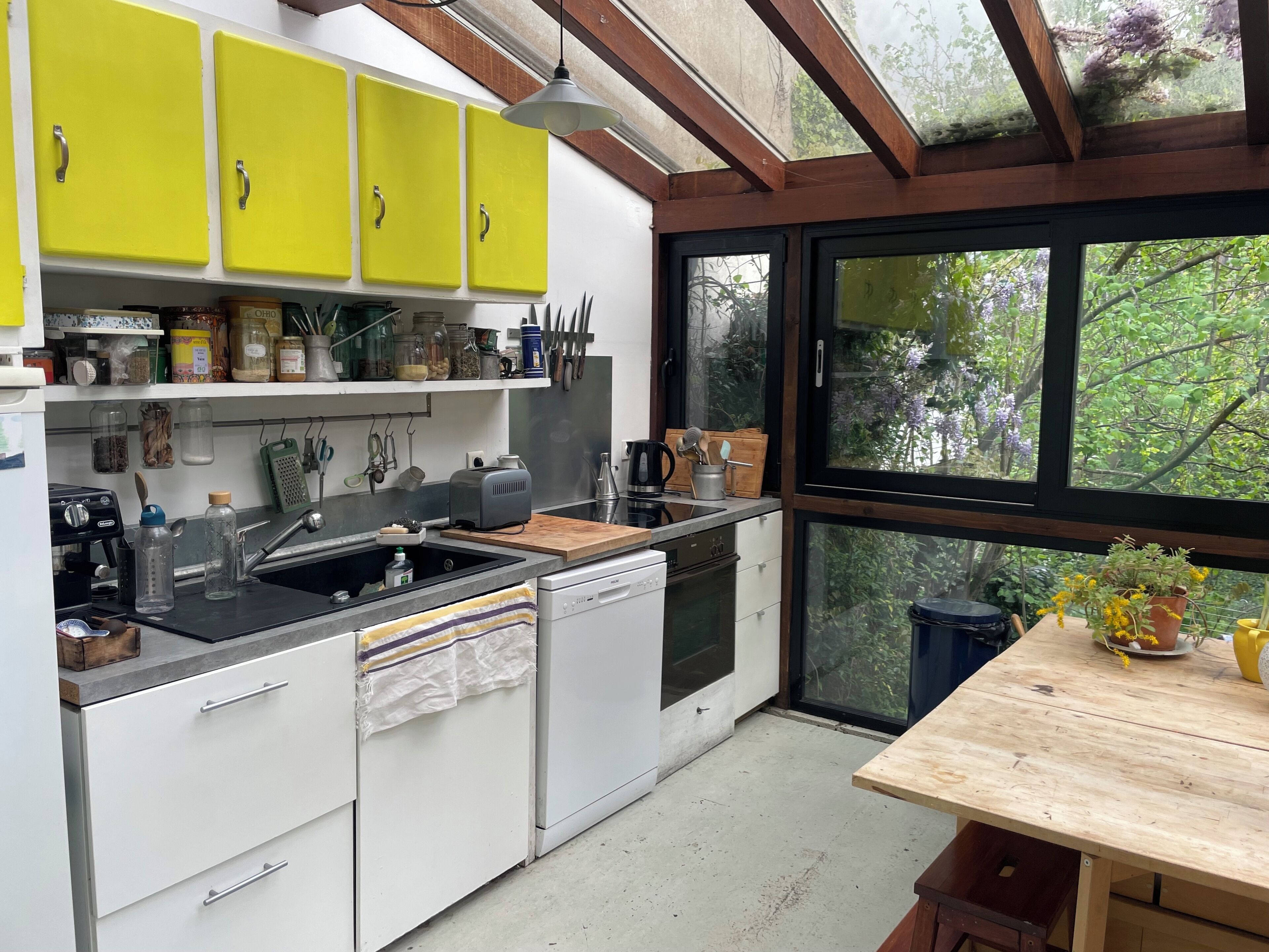 A kitchen with yellow cabinets, a wooden table, and a view of greenery through large windows.