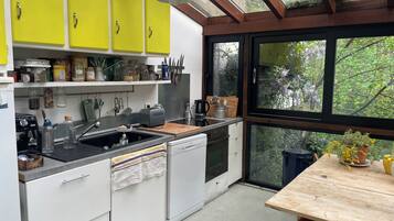 A kitchen with yellow cabinets, a wooden table, and a view of greenery through large windows.