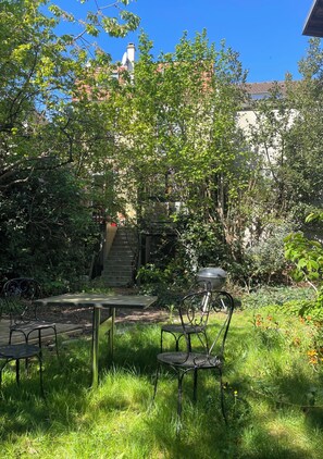 Un jardín con una mesa y sillas, rodeado de follaje y una escalera.