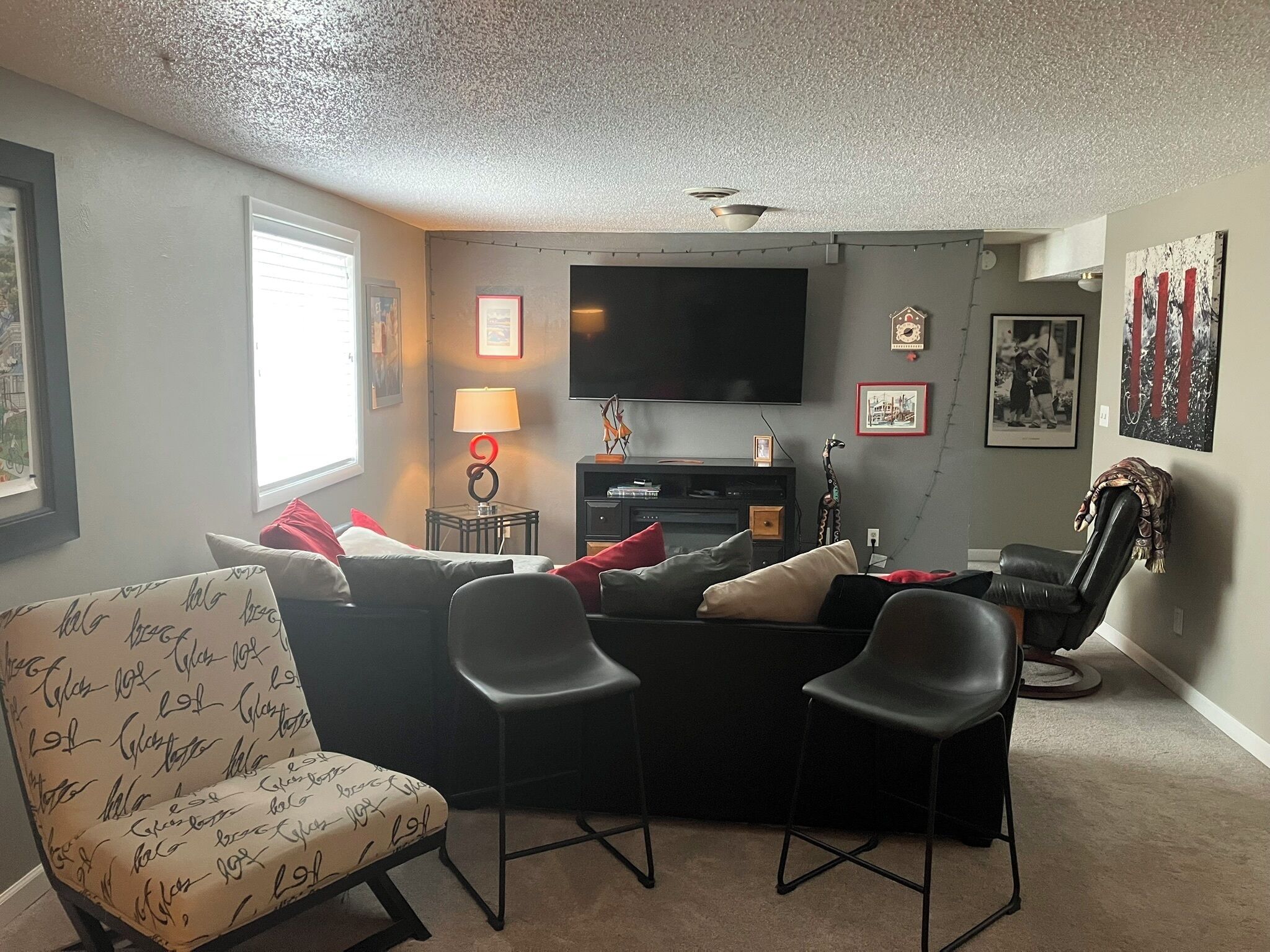 A living room with a sofa, two chairs, a TV, a lamp, and a wall with framed pictures.
