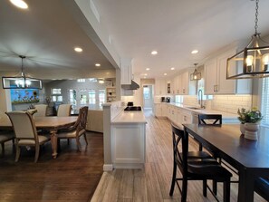 A spacious kitchen with white cabinetry, a central island, and a dining area with wooden chairs. - Gorgeous Villa 10 Mins to Disney (Santa Ana)