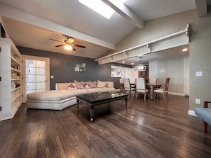 A spacious living room with a dark wood floor, a sofa, a coffee table, and a ceiling fan. - Gorgeous Villa 10 Mins to Disney (Santa Ana)