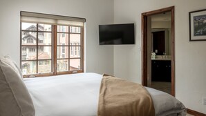 Un dormitorio con cama, televisor, ventana y puerta que da a un baño.