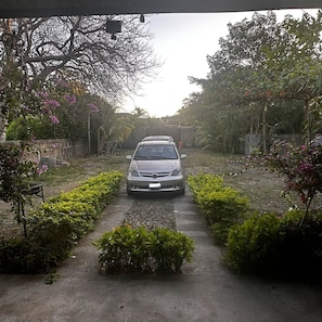 A car parked on a paved path flanked by green hedges and trees. - Casa bella, acogedora y espaciosa cerca del mar. (Pochomil Viejo)
